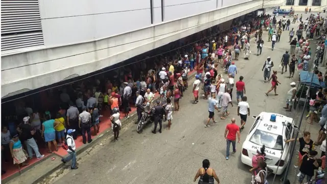 Ciudadanos cubanos haciendo cola para comprar alimentos básicos frente a un mercado.