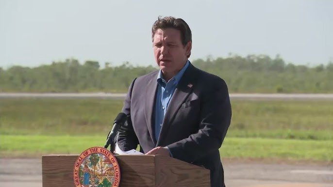 El gobernador Ron DeSantis hablando en un podio frente a las instalaciones de Alligator Alcatraz.